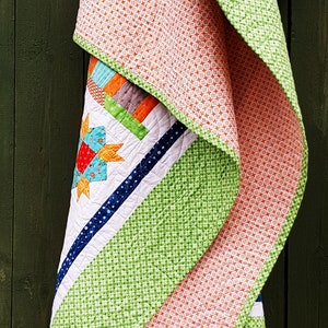 May include: A colorful quilt with a starburst design, featuring orange, green, blue, and white patterns. The quilt has a patchwork design with a variety of geometric shapes and textures. The quilt is folded over, showcasing the different patterns and colors.