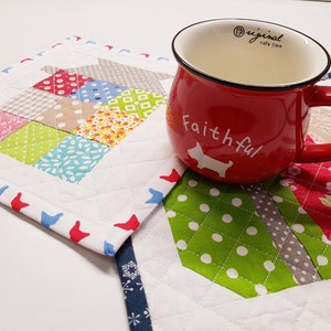 May include: Two colourful quilted fabric coasters with a red mug on top. The mug has a black rim and handle and says "original cafe time" and "Faithful" in white lettering.