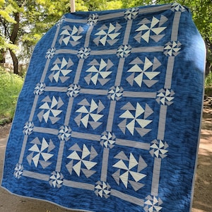 May include: A blue and white quilt with a pinwheel pattern. The quilt is made of cotton fabric and is quilted with a white thread. The quilt is hanging on a clothesline.