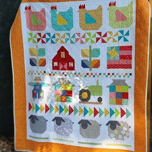 May include: A colorful patchwork quilt featuring a farm theme. The quilt includes images of chickens, a barn, a tractor, a scarecrow, and sheep. The quilt is made with a variety of fabrics in bright colors, including red, yellow, blue, green, and orange.