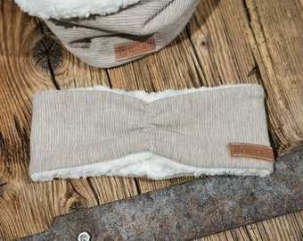 May include: A beige knit headband with a soft white fleece lining. The headband has a brown leather label with the word "Handmade" on it.