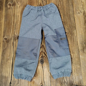 Può includere: Pantaloni grigi per bambini con una toppa su ogni ginocchio e una tasca sulla gamba destra. La tasca ha un piccolo logo che dice "hellomart".