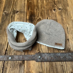 Op de afbeelding: Een bruine fleece nekwarmer en een bruine fleece beanie met een witte stippenvoering. De beanie heeft een bruin lederen label met de tekst "DRECKSPATZ" erop.