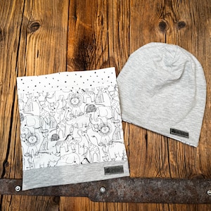 Puede incluir: Un gorro de bebé gris y blanco con estampado de animales en blanco y negro. El gorro está hecho de tela suave y cómoda y tiene un diseño sencillo.