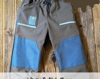 Puede incluir: Pantalones softshell marrones con parches azules en las rodillas, cintura elástica con cordón y tiras reflectantes. Una etiqueta en el bolsillo dice "PECK FRATZ". El texto en la imagen incluye "NEU! Jetzt auch als Softshell mit Fleece" y "Warme Softshellhose für kleine Draußenkinder".