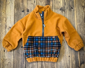 May include: A mustard yellow long-sleeve pullover with a high collar and a dark gray half-zip closure. The garment features a large front pocket with a blue, brown, and white plaid pattern, elasticized cuffs, and a gathered elastic hem.