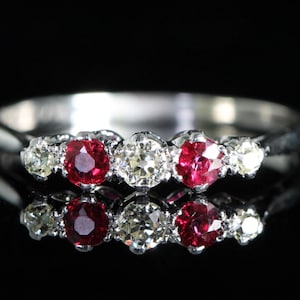 Peut inclure: Une bague en argent ornée de trois pierres rouges vives, encadrées de pierres claires plus petites. Le design de la bague est classique et élégant, avec une finition polie. Les pierres précieuses sont disposées en rang, créant un attrait visuel saisissant.