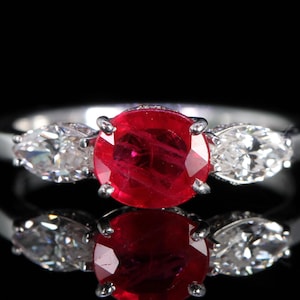 May include: A silver ring with a large, oval-shaped ruby gemstone surrounded by two pear-shaped diamonds.