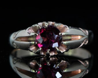 May include: A gold ring with a deep red gemstone set in a decorative, scalloped bezel. The ring has a delicate, ornate design.