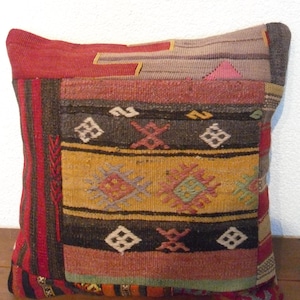 Könnte beinhalten: Ein farbenfrohes Kissen mit einem geometrischen Muster in Rot-, Braun-, Gelb- und Blautönen. Das Kissen ist aus gewebtem Stoff gefertigt und hat ein traditionelles Design.