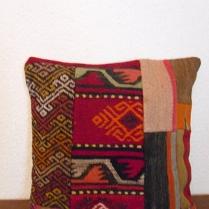 Könnte beinhalten: Ein farbenfrohes Patchwork-Kissen mit geometrischen Mustern in Rot-, Orange-, Braun- und Beigetönen. Das Kissen ist aus gewebtem Stoff und hat einen Fransenrand.