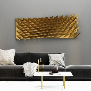 Op de afbeelding: Een moderne woonkamer met een donkergrijze hoekbank, een witte salontafel met gouden poten en een decoratief gouden wandkunstwerk. De kamer is ingericht in neutrale tinten en bevat een witte vaas met takken.