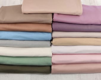 May include: A stack of folded fabric pieces in various solid colors including beige, brown, blue, gray, white, green, pink, and purple. The text Soft · Smooth · Stretchy and BACKDROPS + WRAPS is visible at the top and bottom of the image.