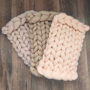 May include: Three chunky knit blankets in shades of pink and beige. The blankets are made of thick yarn and have a soft, fluffy texture.