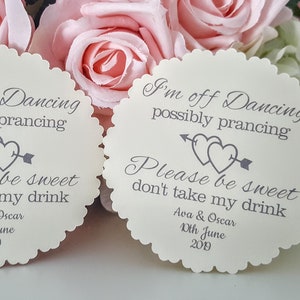 May include: Two white round paper drink coasters with scalloped edges. The coasters have grey text that reads "I'm off Dancing possibly prancing Please be sweet don't take my drink Ava & Oscar 10th June 2019".