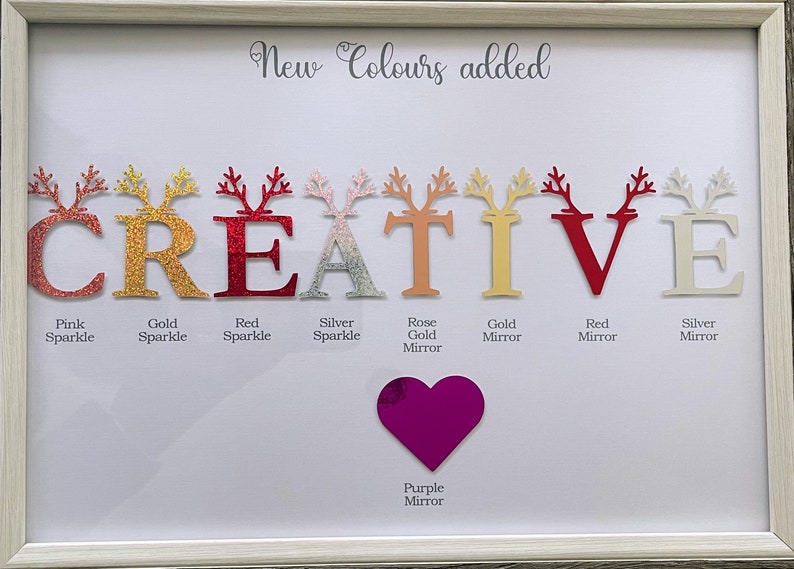 以下が含まれることがあります： 「CREATIVE」という単語がキラキラの文字で書かれた額縁付きのワードアート作品。文字はピンク、ゴールド、レッド、シルバー、ローズゴールド、パープルなど、さまざまな色で書かれています。文字はトナカイの角で飾られています。