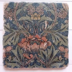 Könnte beinhalten: Eine Vintage-Fliese mit einem floralen Muster in Blautönen, Grün, Orange und Rosa. Die Fliese zeigt eine große zentrale Blume mit filigranen Details und kleinere Blumen und Blätter, die sie umgeben.