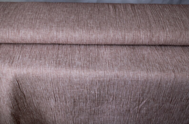 May include: A close-up of a brown fabric with a textured, woven pattern. The fabric is folded in half, showing the texture of the material.