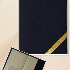May include: A dark blue passport cover with a gold ribbon on the corner. The cover is made of a soft, textured material. The inside of the cover is lined with a red fabric. The cover is open to reveal the inside pages of a passport. The pages are printed with the German coat of arms and text in German.
