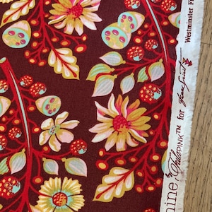 Puede incluir: Tela roja con un patrón floral con flores amarillas, rosas y azules, hojas y bayas. La tela tiene una etiqueta que dice "Moon Shine Plus PINK TM for Frank Garcia" y "Westminster Fibers # PWTP056 Sprout".