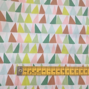 Könnte beinhalten: Weißer Stoff mit einem sich wiederholenden Muster aus bunten Dreiecken in Grün, Braun, Rosa und Blau. Ein gelbes Maßband, mit Zentimetern markiert, liegt auf dem Stoff. Der Text "Made in Germany" ist sichtbar.