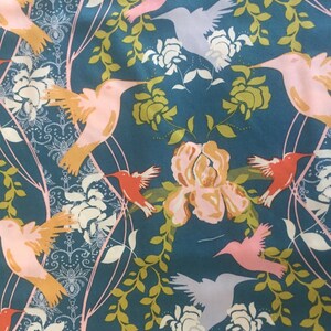 Può includere: Un tessuto blu turchese con un motivo ripetitivo di colibrì rosa e bianchi che volano tra foglie verdi e fiori rosa.