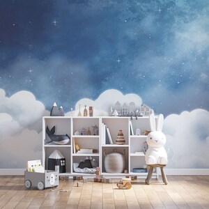 May include: A white bookshelf with various toys and books, including a stuffed bunny, a whale, and a stack of wooden blocks. The bookshelf is in front of a blue and white wall mural depicting a night sky with clouds and stars.