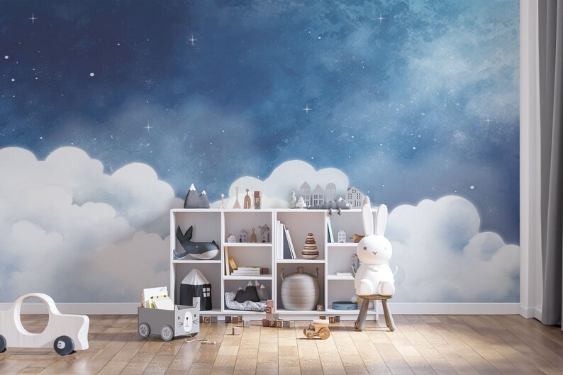 May include: A white bookshelf with various toys and books, including a stuffed bunny, a whale, and a stack of wooden blocks. The bookshelf is in front of a blue and white wall mural depicting a night sky with clouds and stars.