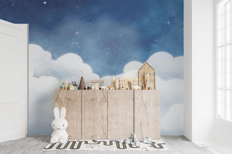 May include: A wooden cabinet with a light wood finish, featuring a row of toy houses and figures against a blue and white starry sky backdrop. The cabinet is in a room with a white door and a white window.
