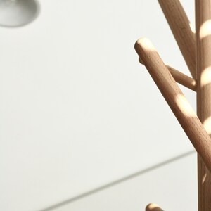 May include: A wooden coat rack with multiple rounded arms extending from a central pole. The rack is made of light-colored wood and is set against a white background. The design is minimalist and modern.