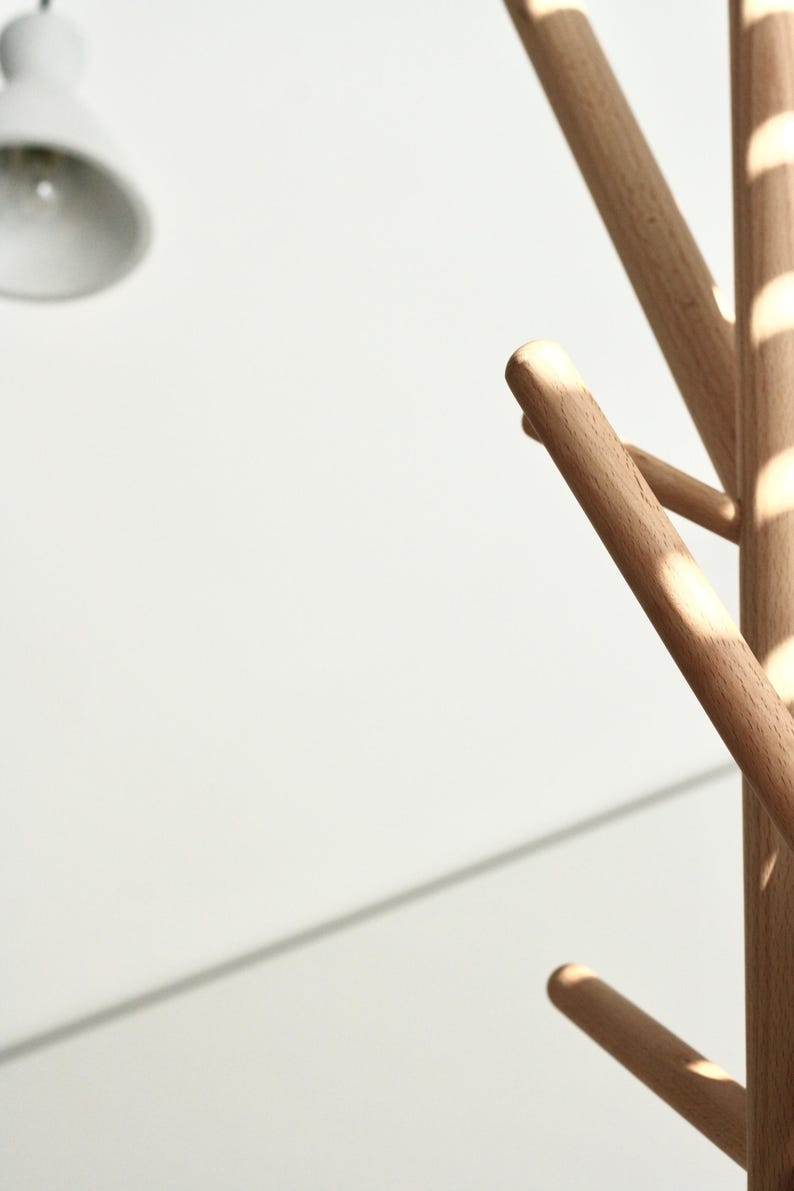 May include: A wooden coat rack with multiple rounded arms extending from a central pole. The rack is made of light-colored wood and is set against a white background. The design is minimalist and modern.