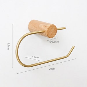 May include: A gold metal toilet paper holder with a wooden base. The holder is 20 cm long, 5.7 cm wide, and 9.7 cm tall. The base is 3.5 cm in diameter.