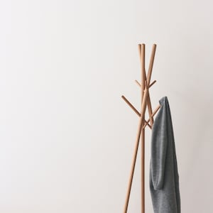 May include: A wooden coat rack with multiple pegs, holding a gray sweater. The rack has a tripod base and a series of upward-reaching pegs. A black and silver industrial-style pendant light hangs above.