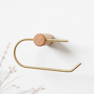 May include: A gold metal towel holder with a wooden base. The holder is mounted to a white wall.
