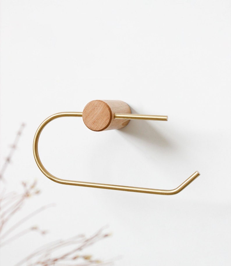 May include: A gold metal towel holder with a wooden base. The holder is mounted to a white wall.