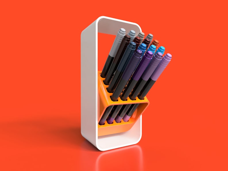 May include: A white stand with an orange holder for coloured markers. The markers are arranged in a fan shape and are mostly shades of blue, purple, and brown.