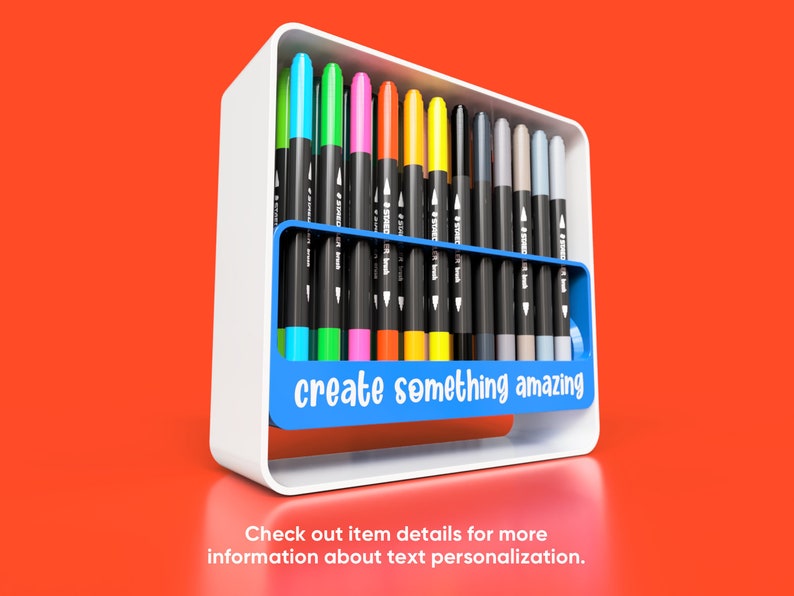 May include: A white holder with a blue section that says "create something amazing" holds a variety of coloured markers.