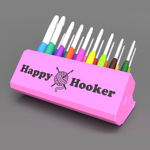 May include: A pink plastic holder with the text "Happy Hooker" and a yarn ball and needles graphic. The holder is filled with a variety of colorful crochet hooks.