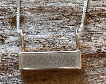 May include: A silver chain necklace with a rectangular pendant featuring a piece of clear, frosted glass.
