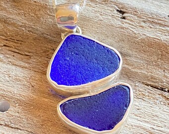 May include: A silver necklace with a pendant made of two pieces of blue sea glass. The sea glass is set in silver and the pendant hangs from a silver chain.