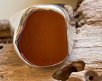 May include: A silver ring featuring a large, rectangular, orange gemstone set in the centre.