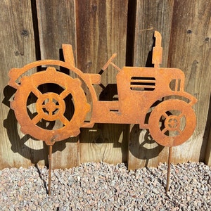 Op de afbeelding: Een roestig metalen silhouet van een tractor met een gedetailleerd wielontwerp. De tractor is gemonteerd op twee metalen palen, perfect voor buitendecoratie in de tuin.