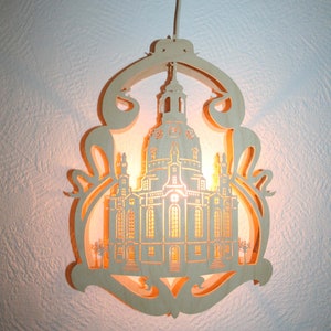May include: A wooden light-up ornament featuring a detailed silhouette of a church with a dome. The ornament is illuminated from within, casting a warm glow.