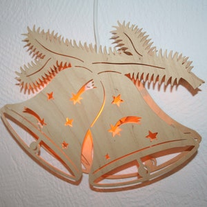 May include: A wooden Christmas ornament shaped like two bells with a star design and a light inside. The bells are hanging from a wooden branch.
