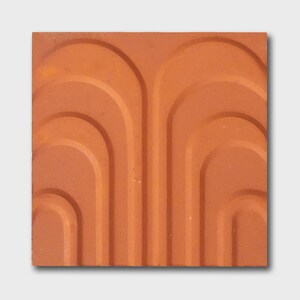 Op de afbeelding: Een terracotta tegel met een herhalend patroon van bogen. De tegel heeft een getextureerd oppervlak en een warme, aardse kleur.