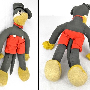 May include: A vintage plush toy of a cartoon character wearing red shorts and a black and white bow tie. The toy has a long, thin tail and is made of felt. The toy is in good condition for its age.