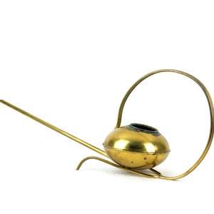 May include: A gold-colored watering can with a long spout and a circular handle. The watering can is made of metal and has a shiny finish.