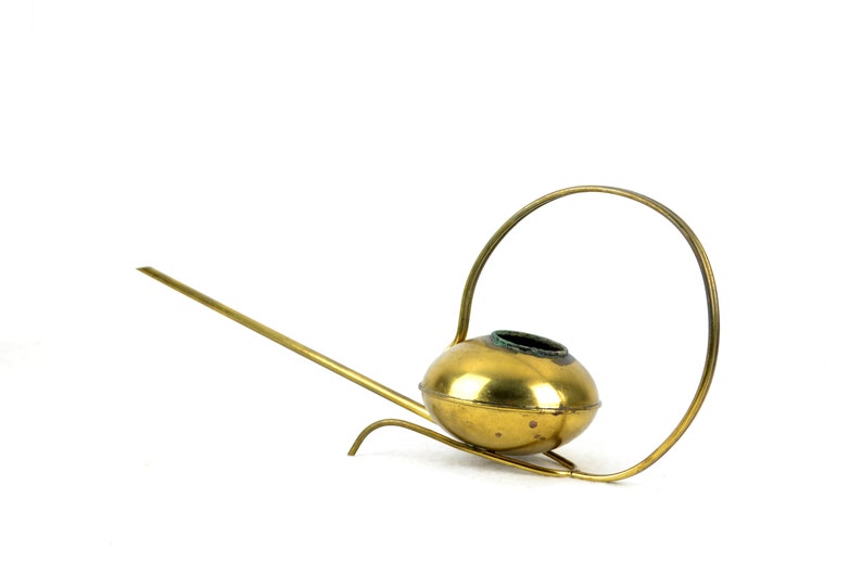 May include: A gold-colored watering can with a long spout and a circular handle. The watering can is made of metal and has a shiny finish.