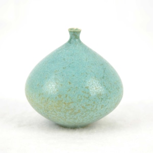 Può includere: Un vaso in ceramica turchese con corpo arrotondato e collo stretto. Il vaso ha una texture maculata con riflessi dorati ed è posto su uno sfondo bianco. La forma generale ricorda una goccia.