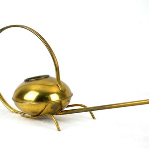 May include: A brass watering can with a long spout and a curved handle. The watering can has a round body and a decorative base.